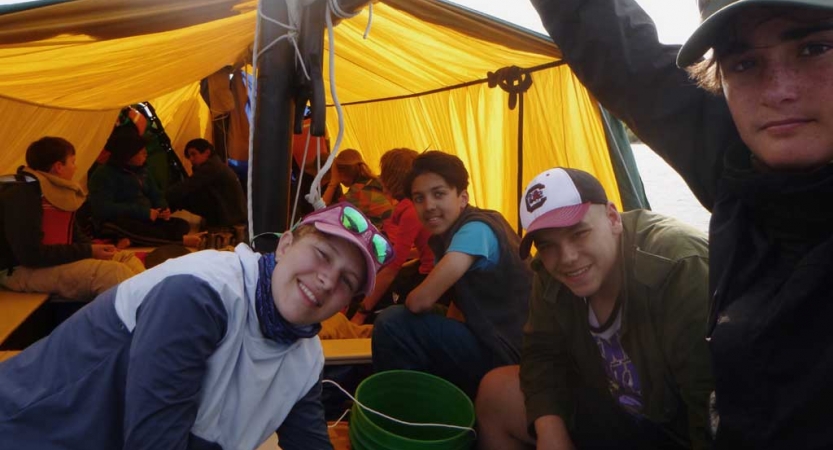 A group of people sitting under a tarp smile for the photo. 